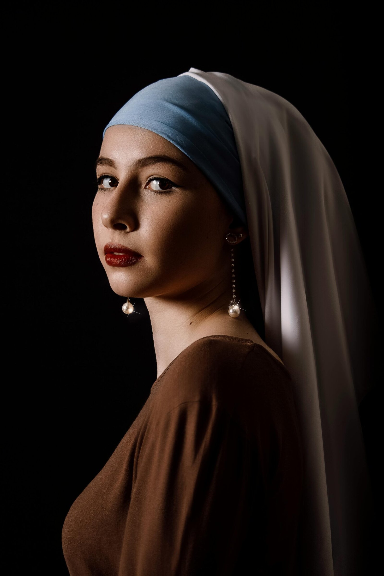 A woman in a headscarf and earrings poses gracefully in low light, showcasing elegance and poise.